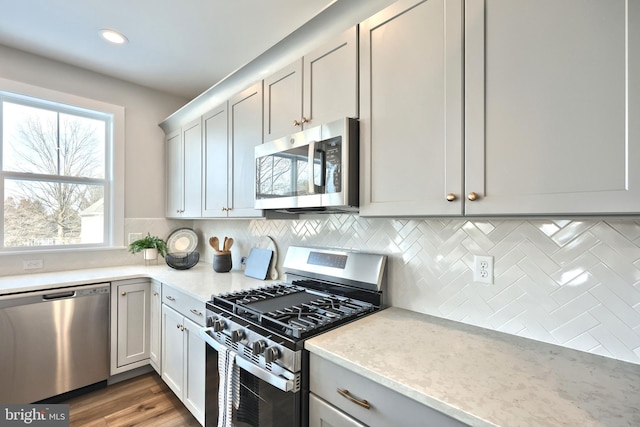 kitchen with light wood finished floors, appliances with stainless steel finishes, light stone countertops, backsplash, and recessed lighting