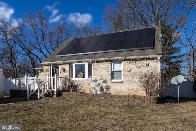 view of front of property featuring brick siding, roof with shingles, a front lawn, and roof mounted solar panels