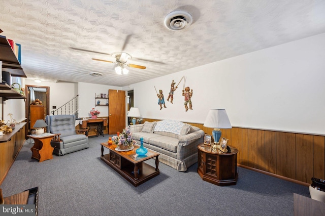 carpeted living area with visible vents, a wainscoted wall, stairs, a textured ceiling, and wood walls