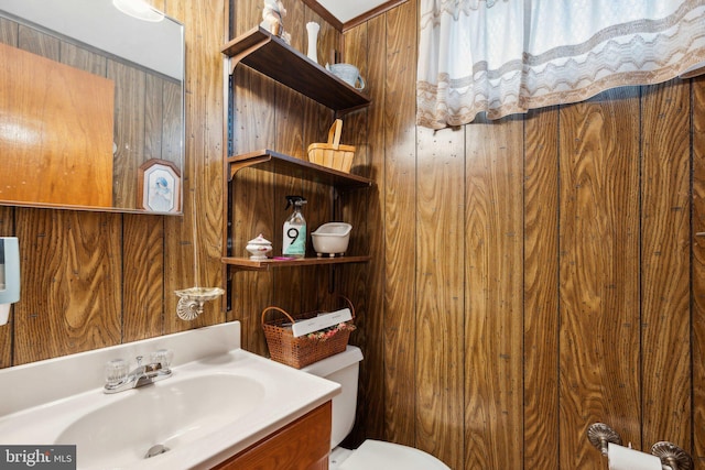 bathroom with toilet, wooden walls, and vanity