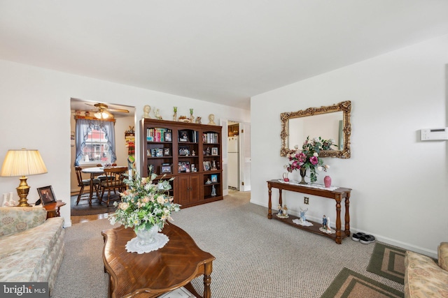 carpeted living area with a ceiling fan and baseboards