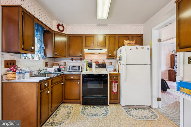 kitchen featuring freestanding refrigerator, light countertops, under cabinet range hood, a sink, and range with electric stovetop