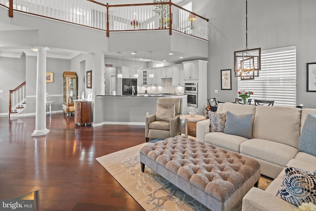 living room featuring a notable chandelier, ornamental molding, dark wood-type flooring, and ornate columns