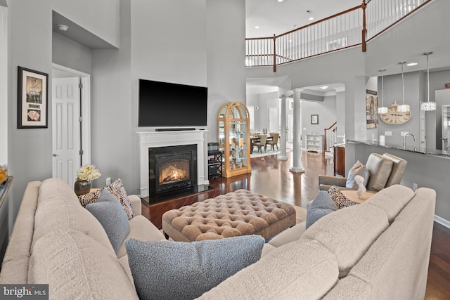 living room featuring decorative columns, dark wood-type flooring, sink, and a towering ceiling