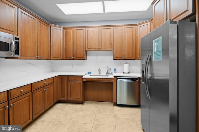 kitchen with appliances with stainless steel finishes, sink, light stone counters, and decorative backsplash