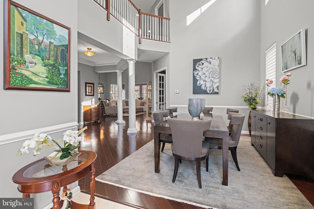 dining room with hardwood / wood-style floors, decorative columns, a high ceiling, and ornamental molding