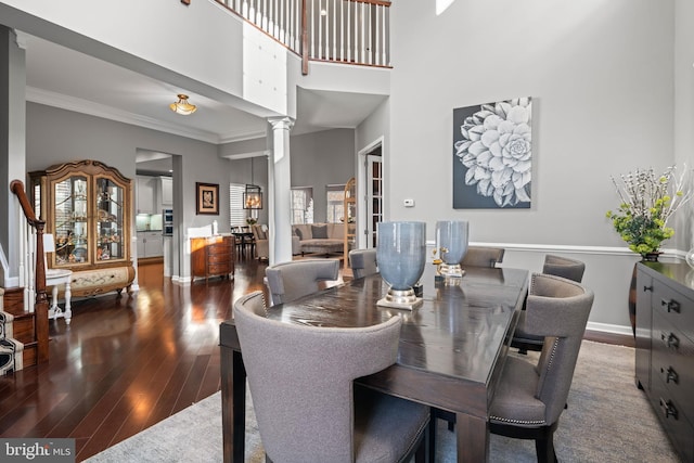 dining space featuring crown molding, wood-type flooring, a towering ceiling, and ornate columns