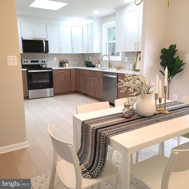 kitchen featuring tasteful backsplash, light countertops, stainless steel appliances, white cabinetry, and a sink