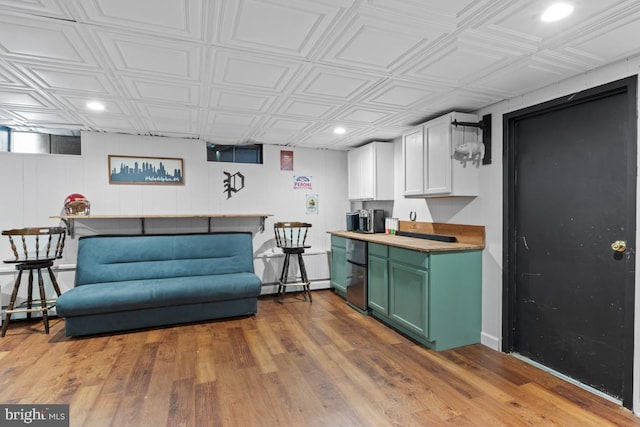 interior space featuring butcher block countertops, a kitchen breakfast bar, green cabinets, light hardwood / wood-style floors, and white cabinets