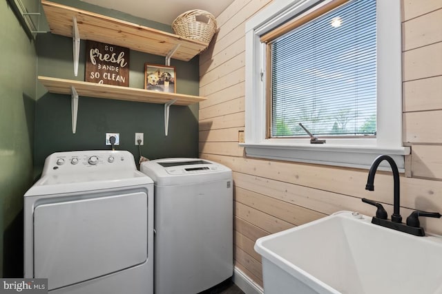 laundry area featuring sink, wooden walls, and washing machine and dryer