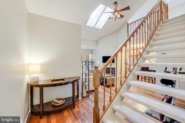 stairs with a skylight, high vaulted ceiling, a textured ceiling, ceiling fan, and hardwood / wood-style floors