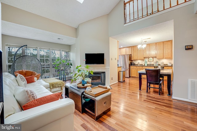 living room featuring an inviting chandelier, a textured ceiling, light wood-type flooring, a towering ceiling, and a fireplace