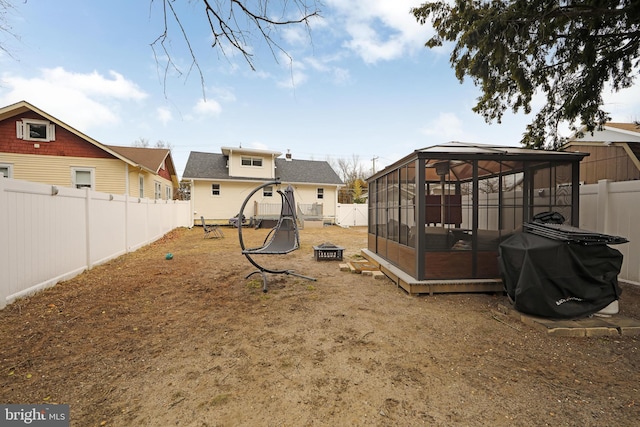 view of yard featuring a sunroom, a fenced backyard, and a fire pit