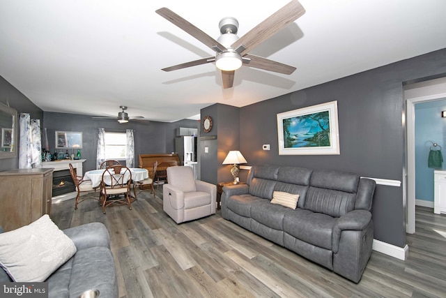 living area with ceiling fan, wood finished floors, a glass covered fireplace, and baseboards