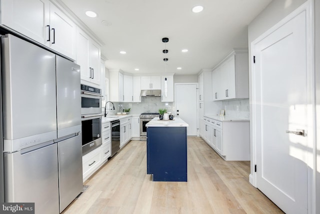 kitchen with light wood finished floors, stainless steel appliances, white cabinets, a sink, and under cabinet range hood