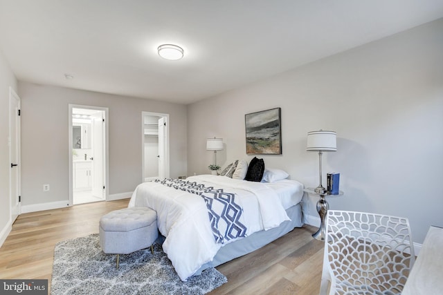 bedroom with ensuite bathroom, a walk in closet, light wood-style flooring, and baseboards