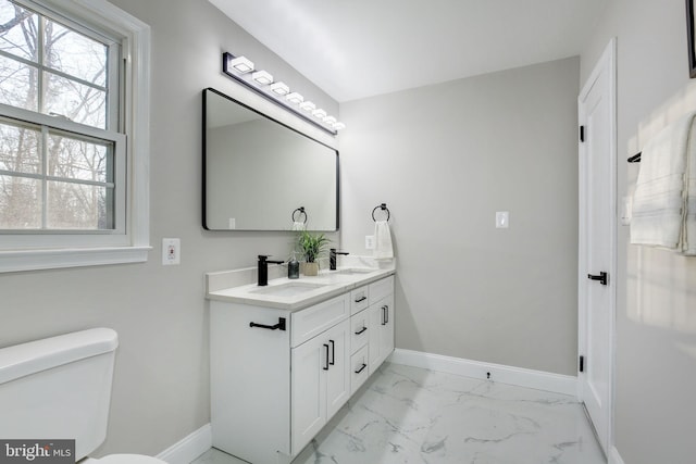 bathroom featuring marble finish floor, double vanity, toilet, a sink, and baseboards