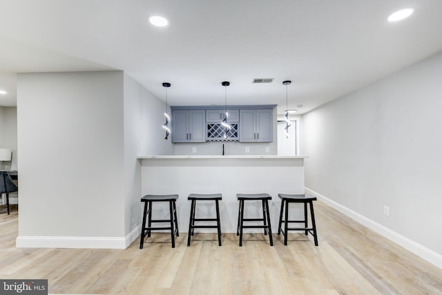 kitchen featuring a peninsula, a breakfast bar, visible vents, baseboards, and light wood finished floors