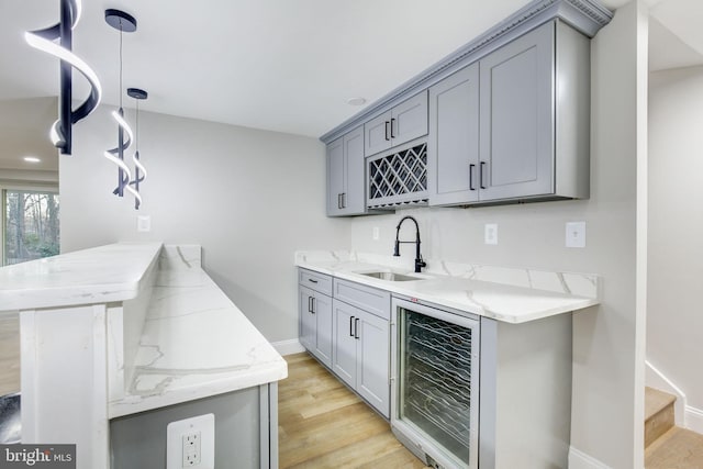 bar with beverage cooler, a sink, baseboards, light wood-type flooring, and indoor wet bar