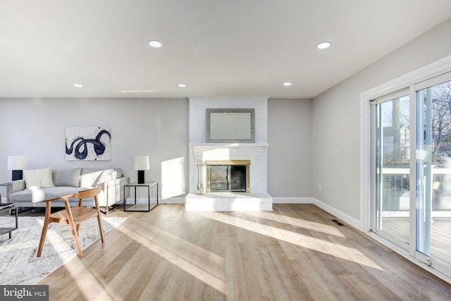 living area with visible vents, baseboards, wood finished floors, a brick fireplace, and recessed lighting