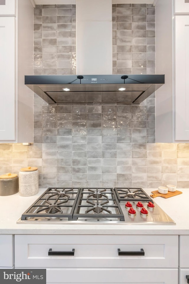 kitchen featuring tasteful backsplash, stainless steel gas cooktop, white cabinets, and wall chimney exhaust hood