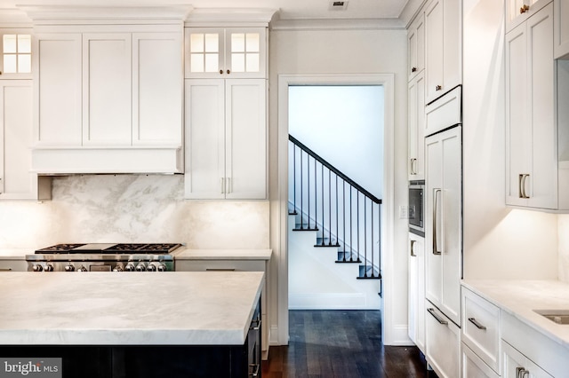 kitchen with dark hardwood / wood-style floors, tasteful backsplash, white cabinets, built in appliances, and light stone countertops