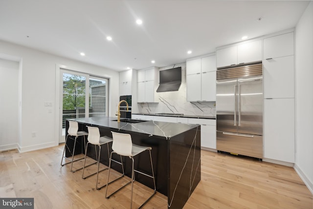 kitchen with wall chimney exhaust hood, a kitchen bar, sink, appliances with stainless steel finishes, and a kitchen island with sink