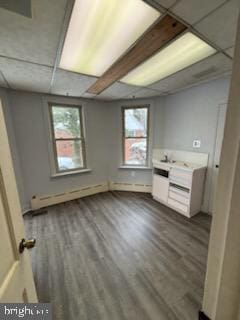 unfurnished bedroom with dark wood-style floors, baseboard heating, and a drop ceiling