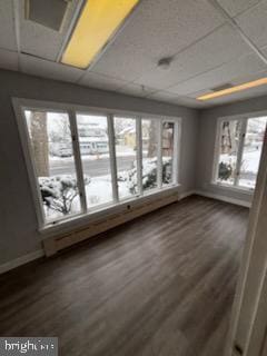 empty room featuring dark wood-type flooring, a drop ceiling, and plenty of natural light