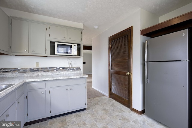 kitchen featuring light countertops, white microwave, gray cabinets, and freestanding refrigerator