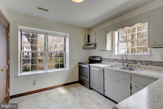 kitchen with stainless steel appliances, a sink, visible vents, light countertops, and ventilation hood