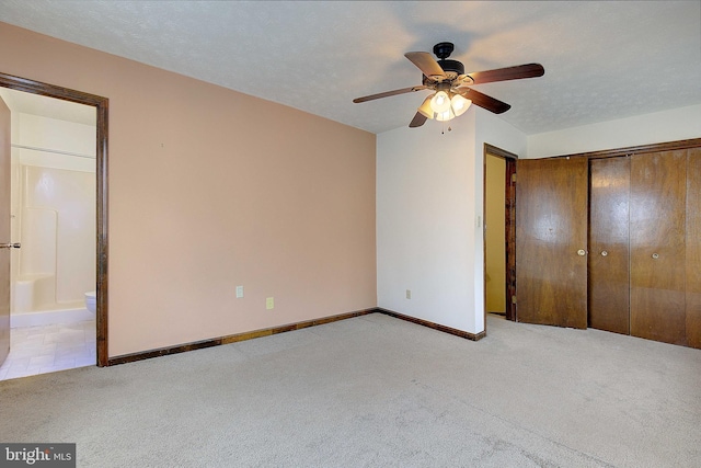 unfurnished bedroom featuring baseboards, connected bathroom, light colored carpet, a textured ceiling, and a closet