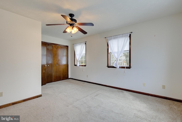 unfurnished bedroom with a ceiling fan, a closet, light colored carpet, and baseboards