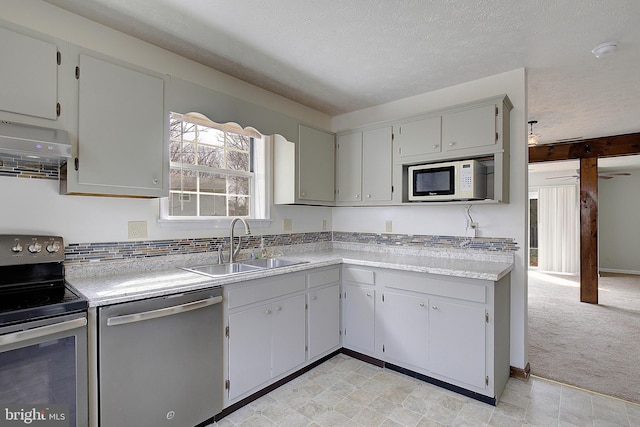 kitchen with light colored carpet, wall chimney exhaust hood, appliances with stainless steel finishes, light countertops, and a sink