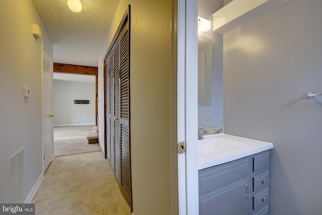 corridor featuring visible vents, a sink, a textured ceiling, and baseboards