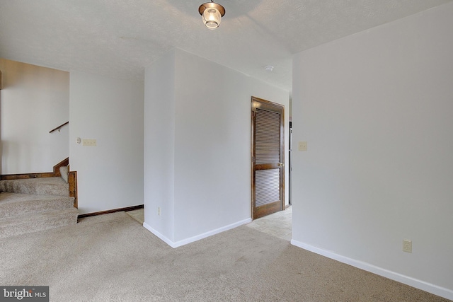 empty room with light carpet, stairway, baseboards, and a textured ceiling