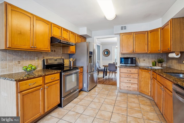 kitchen with light tile patterned floors, visible vents, dark stone counters, appliances with stainless steel finishes, and under cabinet range hood