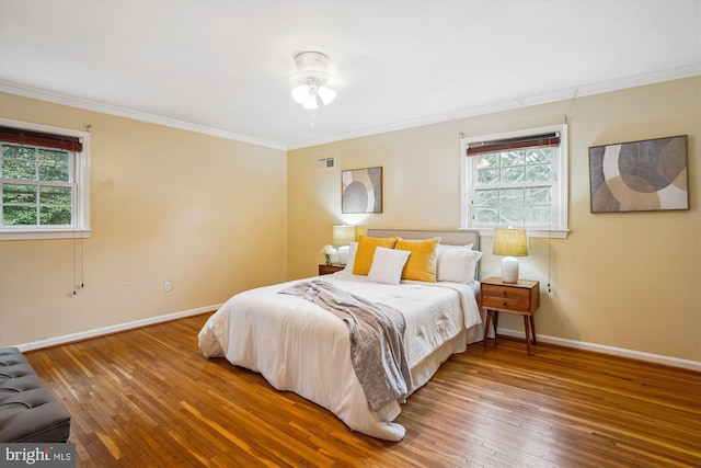 bedroom with crown molding, wood finished floors, visible vents, and baseboards