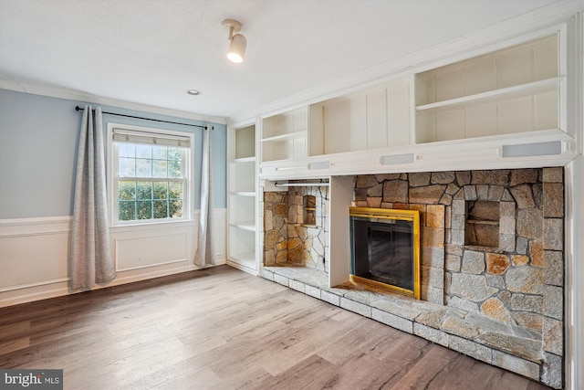 unfurnished living room with built in features, a wainscoted wall, ornamental molding, wood finished floors, and a fireplace