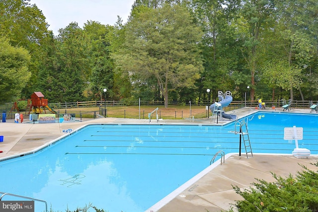 community pool with playground community, a water slide, a patio area, and fence