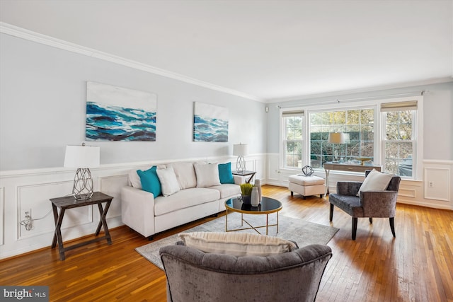 living room with a wainscoted wall, crown molding, a decorative wall, and wood finished floors