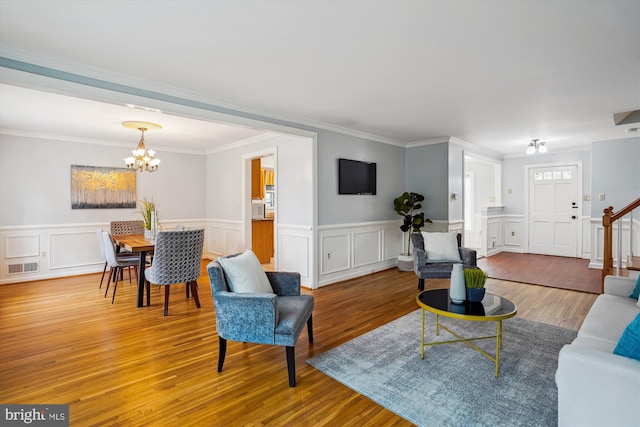 living area with crown molding, visible vents, an inviting chandelier, wood finished floors, and stairs