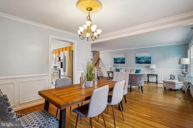 dining space featuring crown molding, a notable chandelier, a decorative wall, wainscoting, and wood finished floors