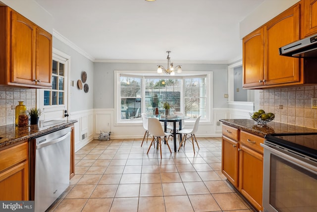 kitchen featuring light tile patterned floors, wainscoting, appliances with stainless steel finishes, and dark stone countertops