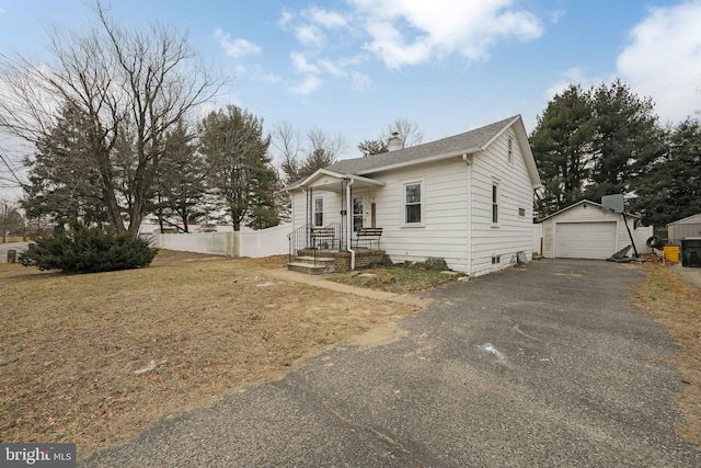 view of front of property featuring aphalt driveway, an outdoor structure, fence, a detached garage, and a chimney