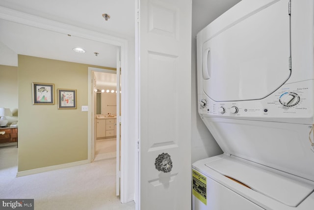 clothes washing area featuring light carpet, laundry area, stacked washer / dryer, and baseboards