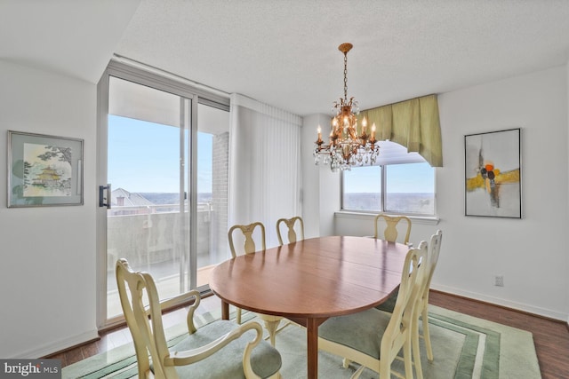 dining room with a notable chandelier, a textured ceiling, wood finished floors, a wall of windows, and baseboards