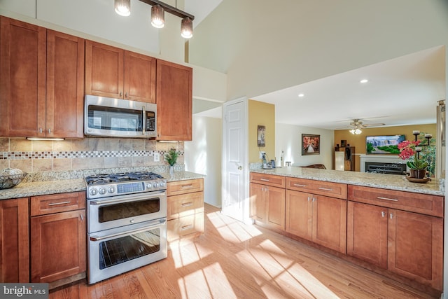 kitchen featuring light wood-type flooring, appliances with stainless steel finishes, decorative backsplash, and a ceiling fan