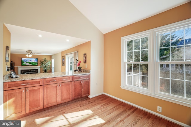 kitchen featuring vaulted ceiling, brown cabinetry, light wood-style flooring, and light stone countertops