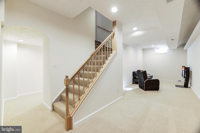 stairway with arched walkways, a textured ceiling, carpet flooring, and baseboards